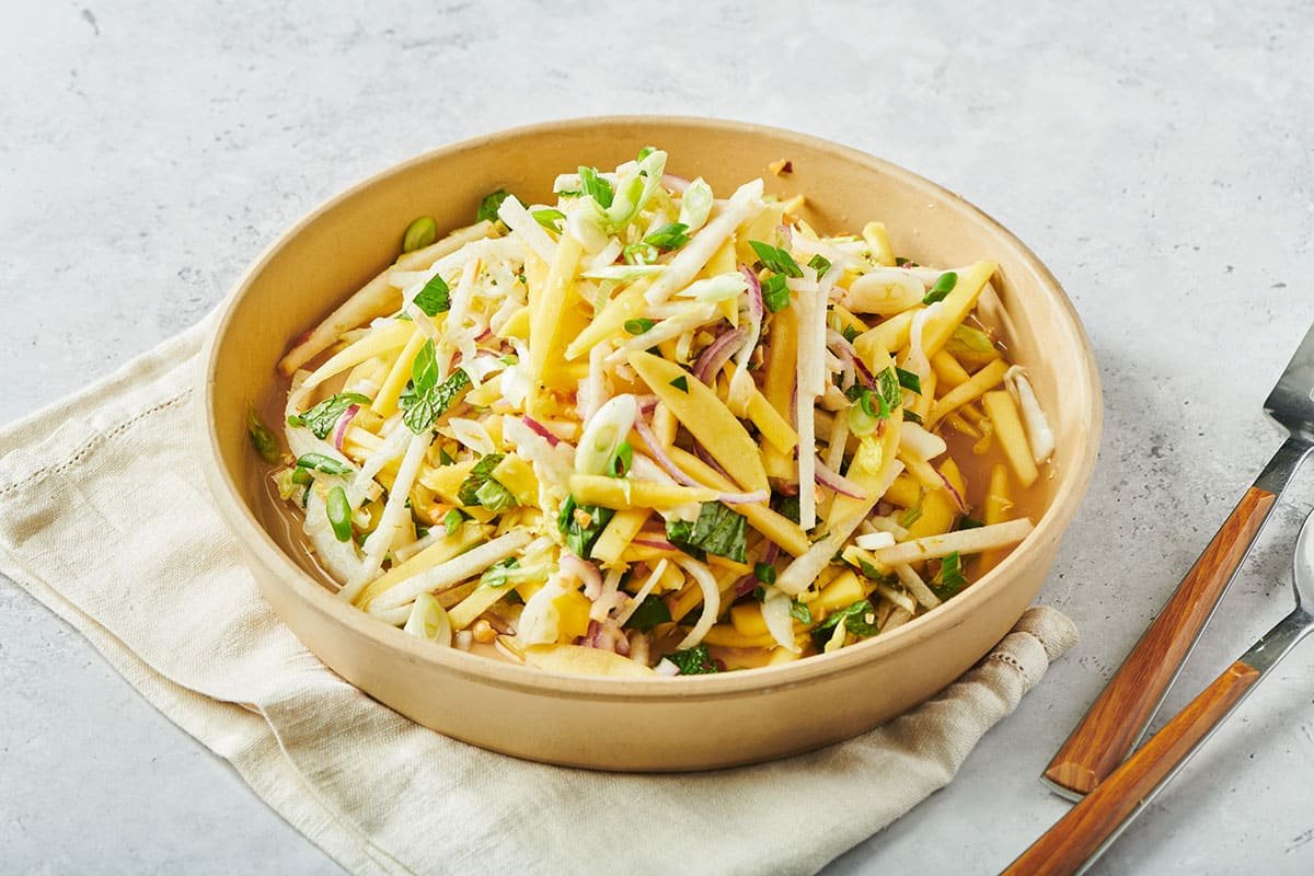 Vietnamese green mango salad in brown bowl on table.