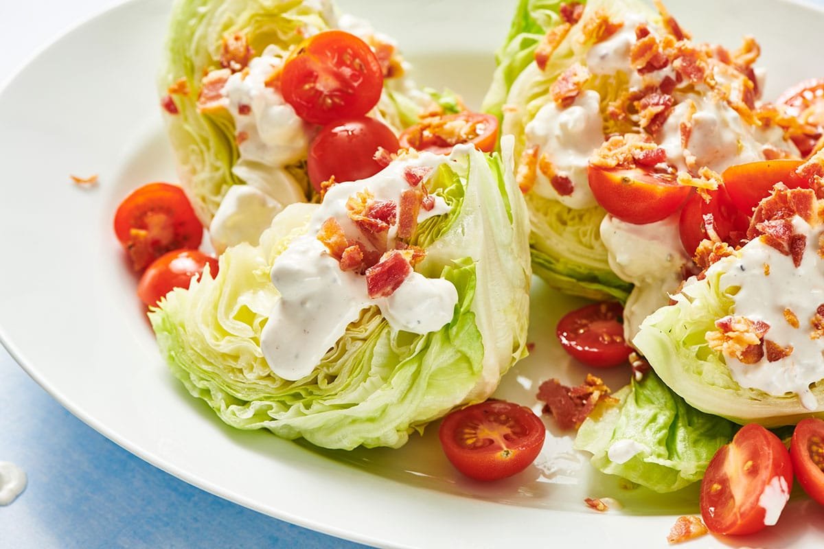 Classic wedge salad with tomatoes, bacon, cheese, and dressing on plate.